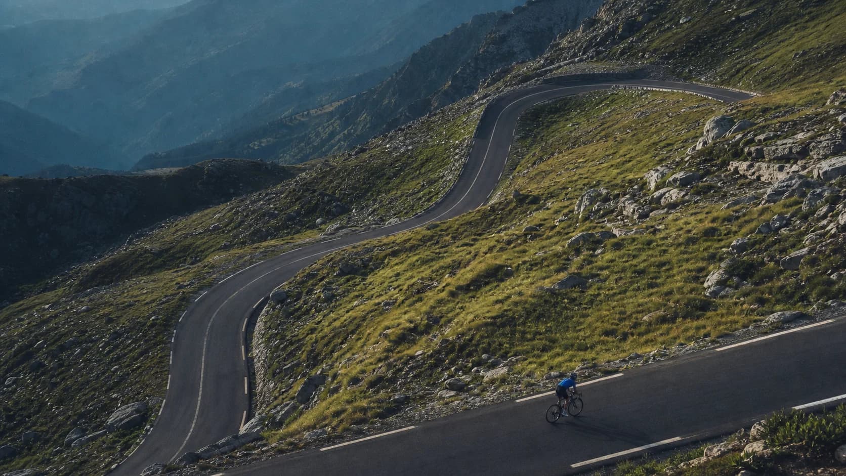 A cyclist following a winding road through a mountain pass